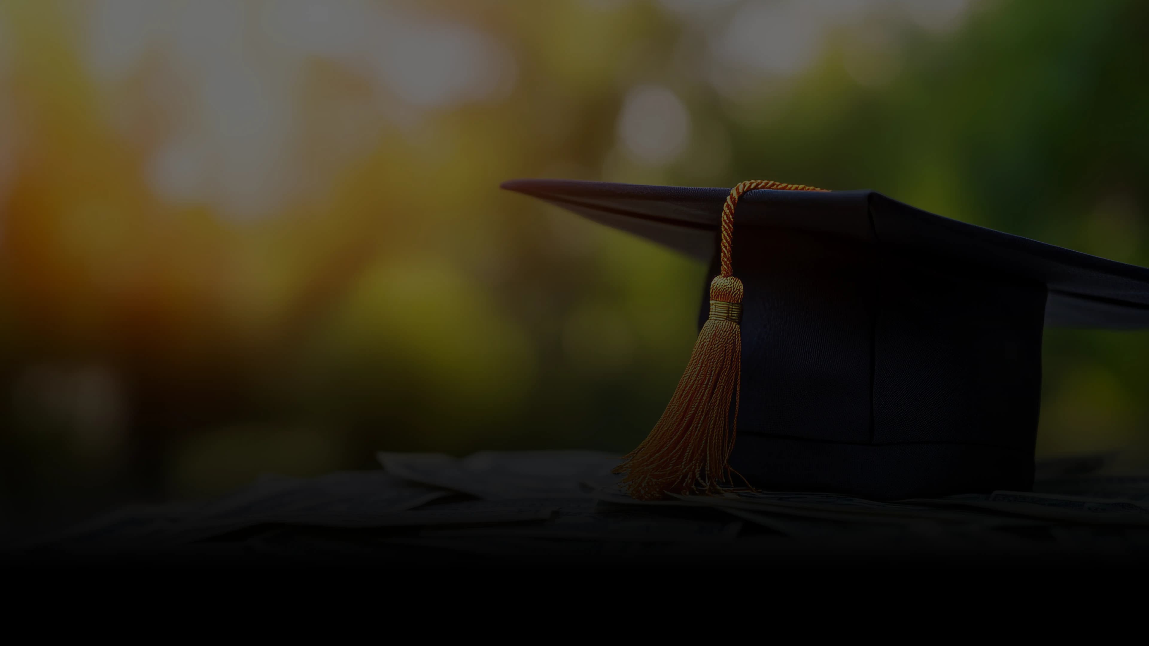 Graduation cap with gold tassel on a dark campus backdrop